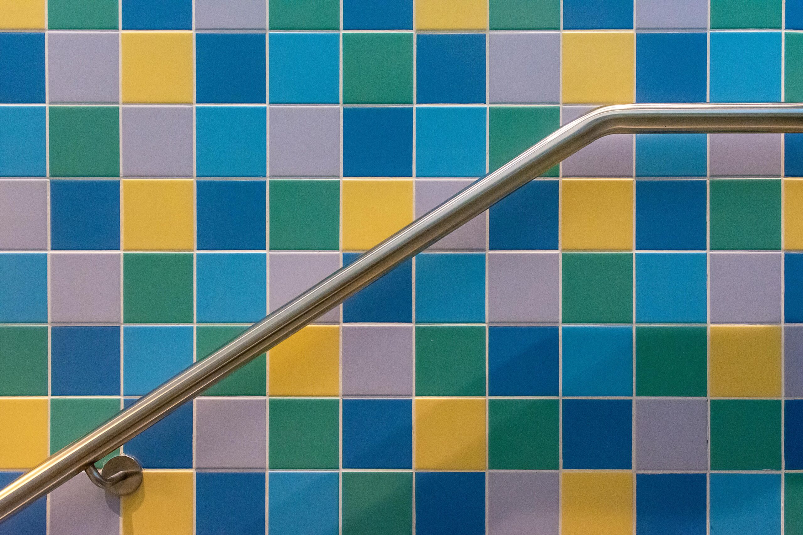 Vibrant square tiles in blue, yellow, and green with a sleek stainless steel railing.